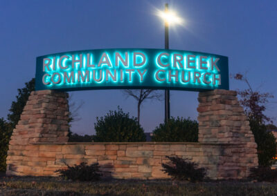 "An illuminated archway sign for Richland Creek Community Church with teal blue lighting and stone pillars set against a twilight sky."