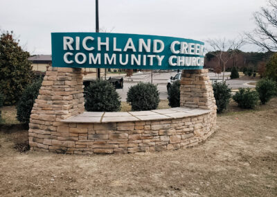 "Daytime view of Richland Creek Community Church sign with teal lettering on a curved stone wall, conveying a welcoming entrance."
