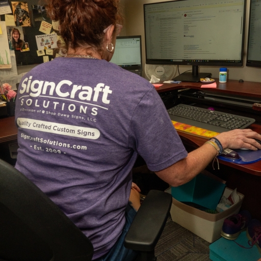 A SignCraft Solutions employee focused on her work at a computer desk, wearing a company branded T-shirt.